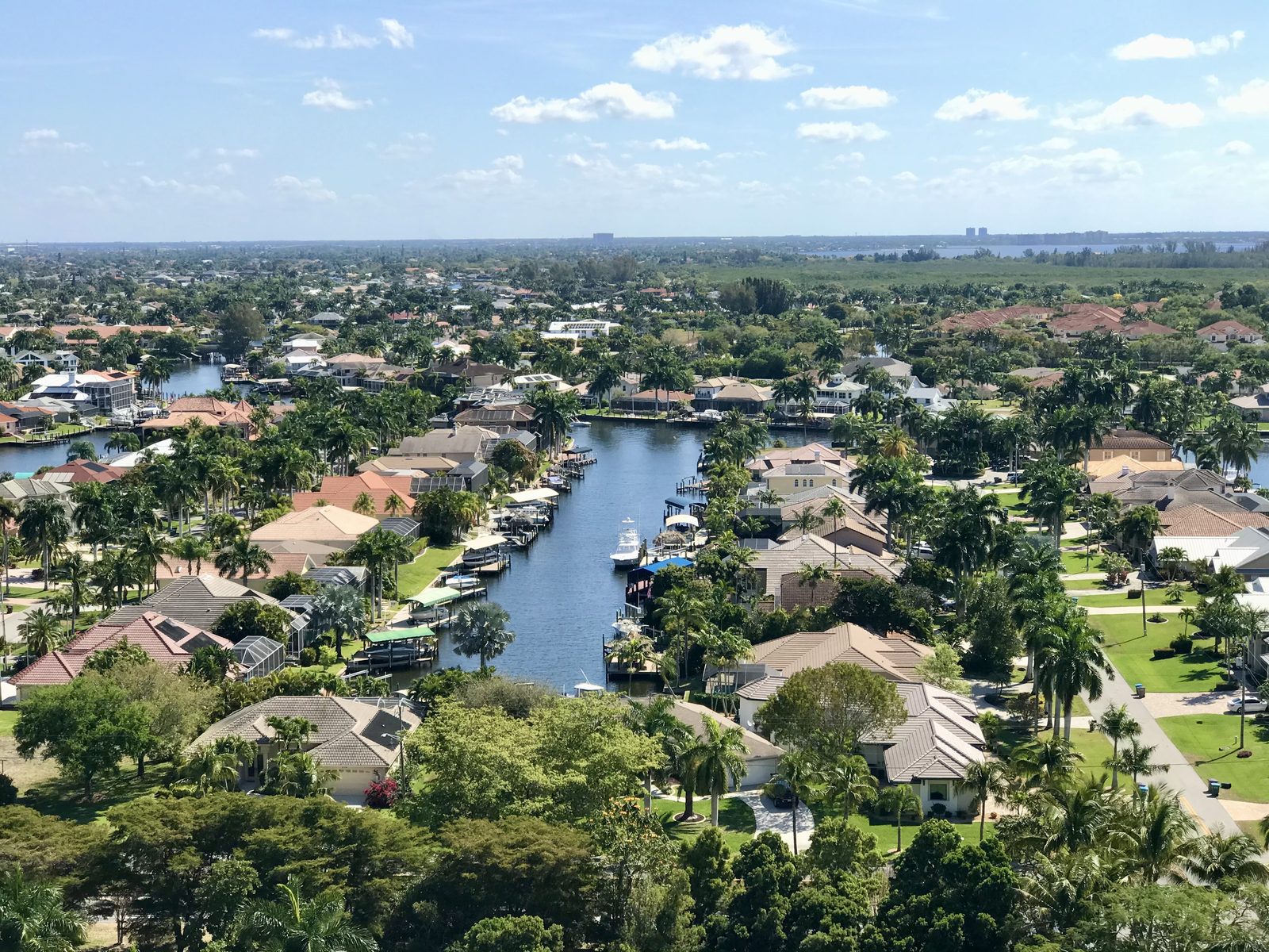 Aerial view over Cape Coral: a wide canal lined with docks, boat lifts and palm trees, houses on both banks.